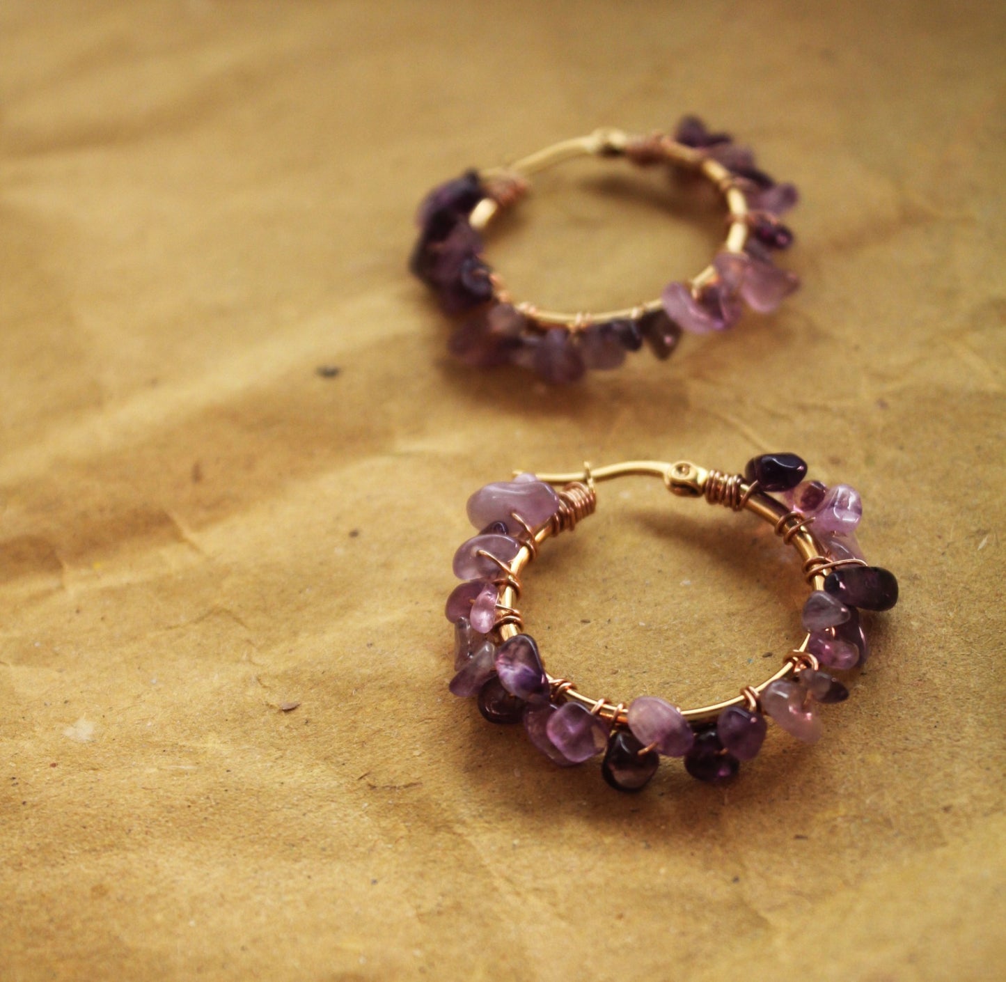 Close up of natural amethyst gemstones on gold hoop earrings, deep purple crystal details